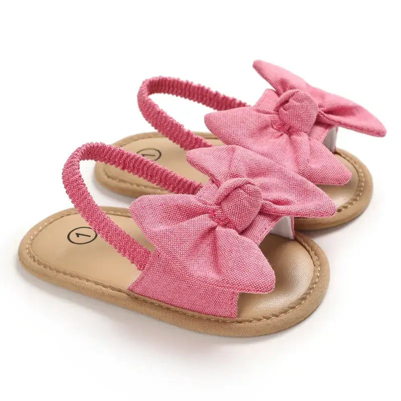 Rose pink baby sandals with large bow detail, open toe and elasticated ruched ankle strap
