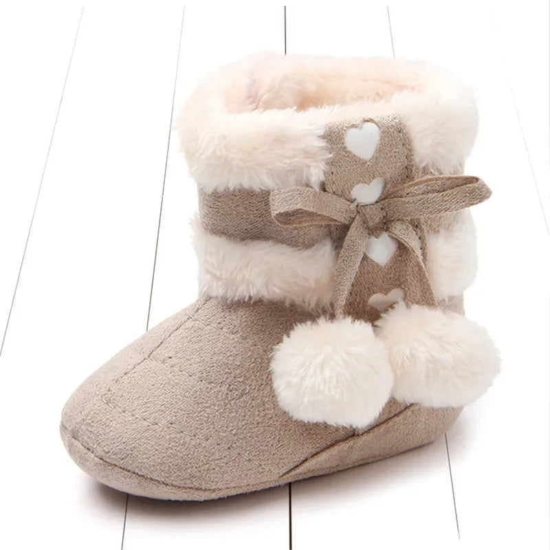 Soft heart slipper boots for babies featuring plush fur lining, heart details, and pom poms in fawn