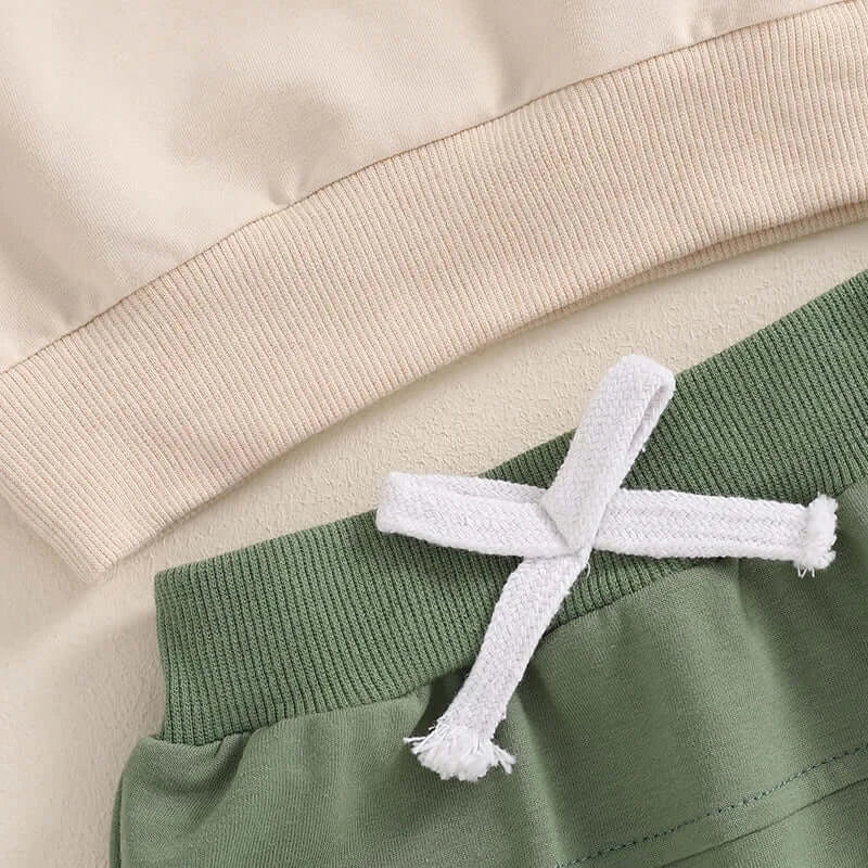 Detail shot of the drawstring waistband aon the green tracksuit bottoms, with the beige pullover hem.