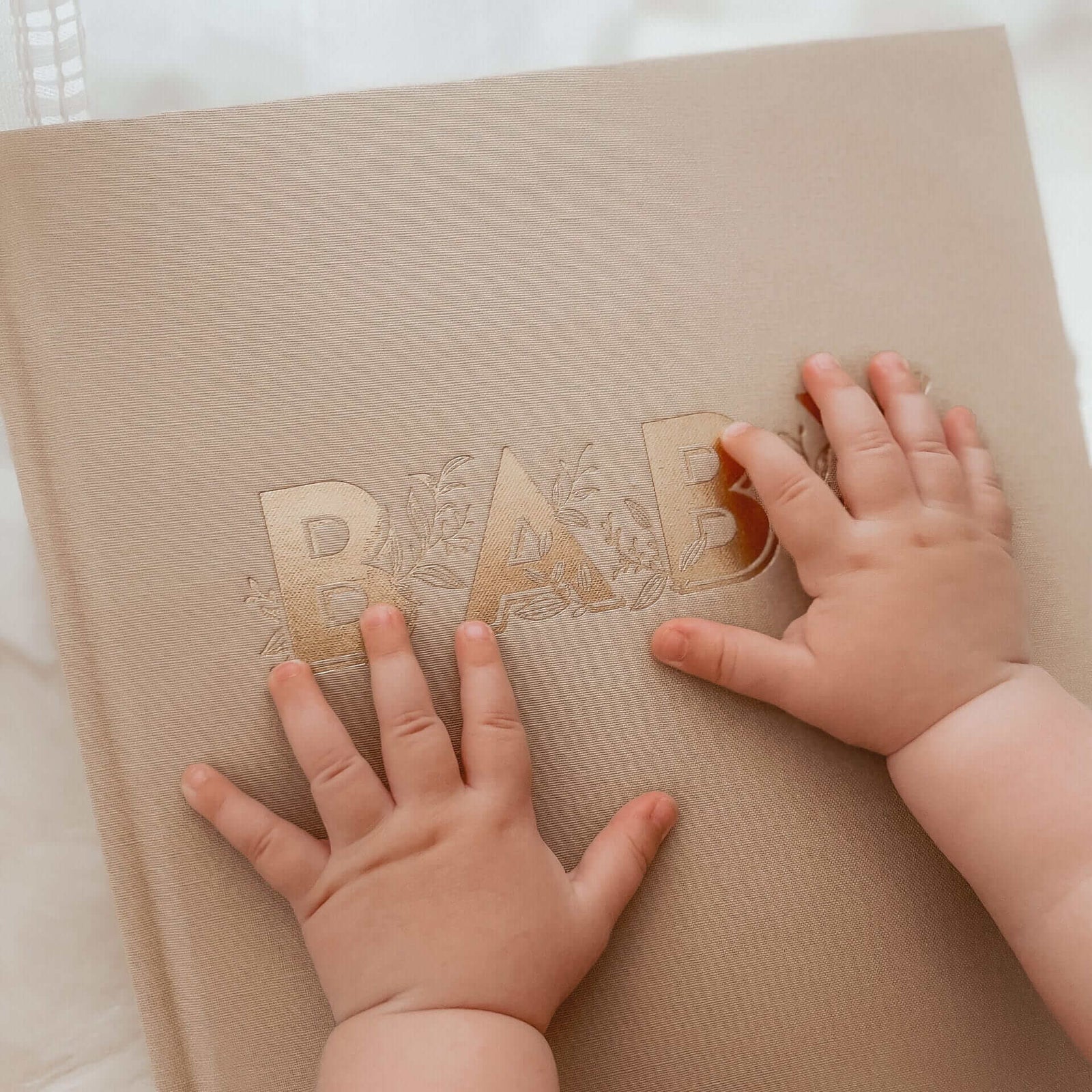 Baby's hands on keepsake journal in biscuit colour, for recording milestones and memories