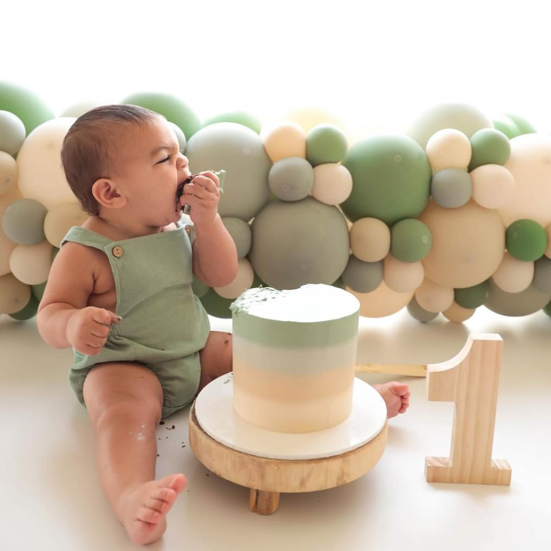 Baby boy wearing sleeveless green baby romper for his cake smash photo shoot.