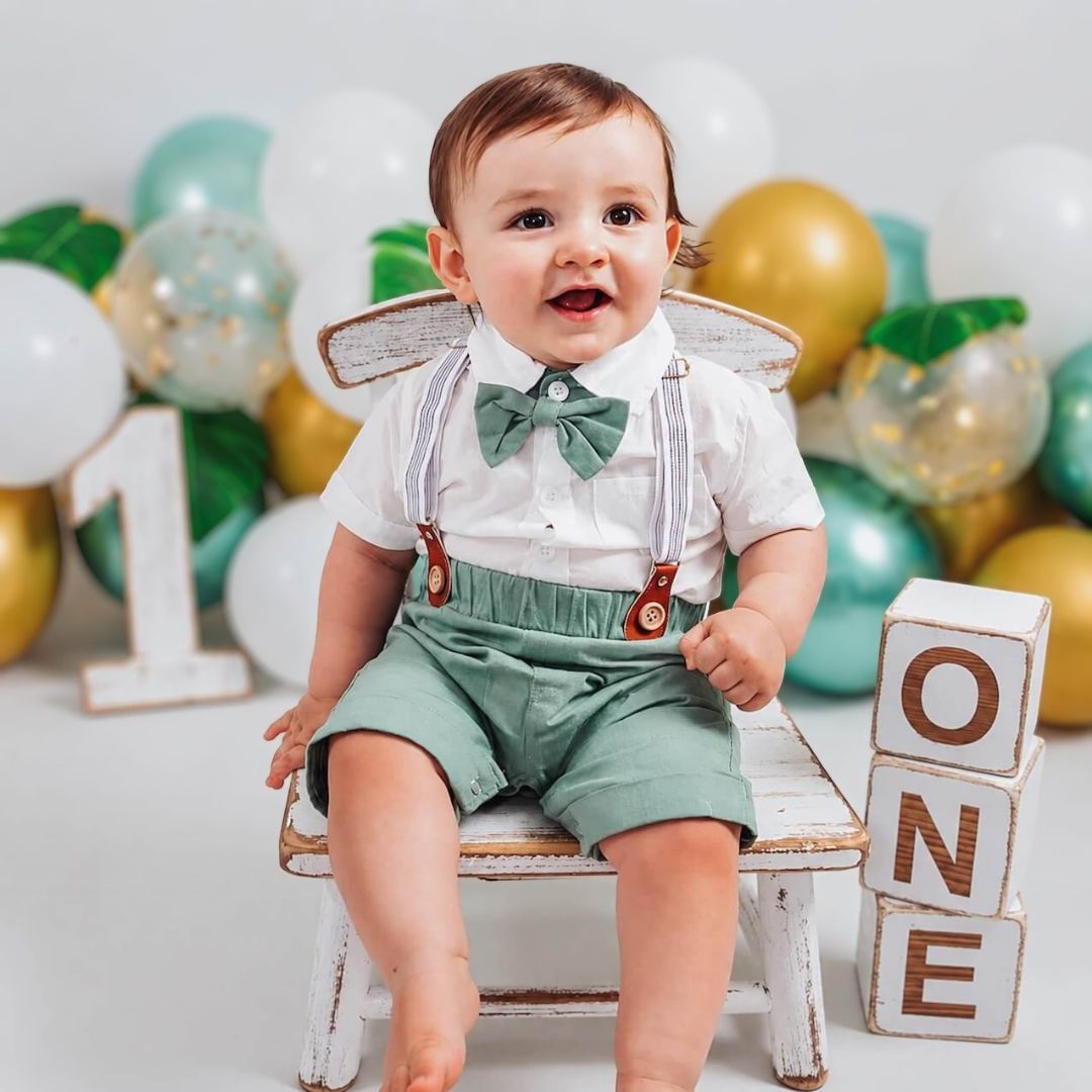 Baby boy wearing green suspender shorts and bow tie set for this first birthday party
