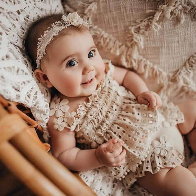 Smiling baby wearing an adorable baby girl outfit - a boho lace set including beige sleeveless top and matching bloomer shorts with delicate floral details.