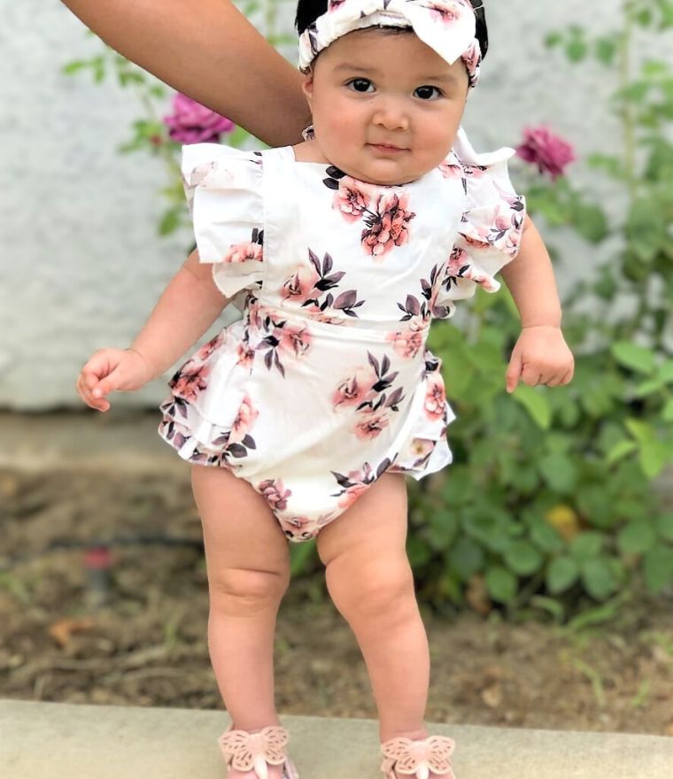 Baby girl wearing white floral ruffle romper with matching headband