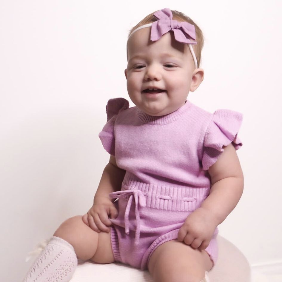 Smiling baby girl wearing purple ruffle knit baby romper from Lulu Babe