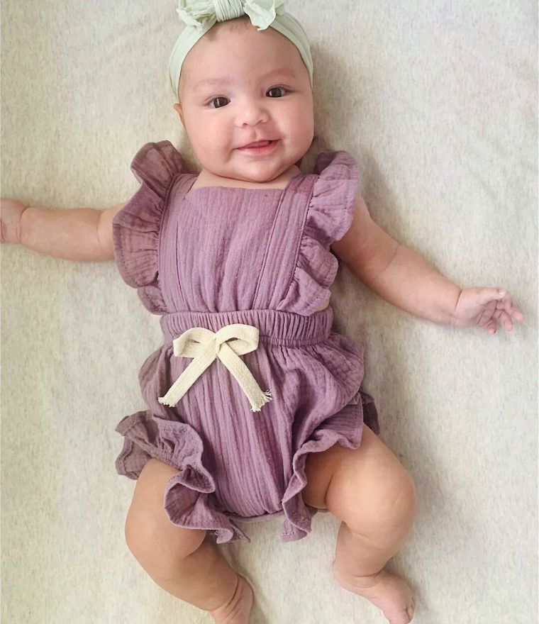 Baby girl wearing purple ruffle romper laying on bed