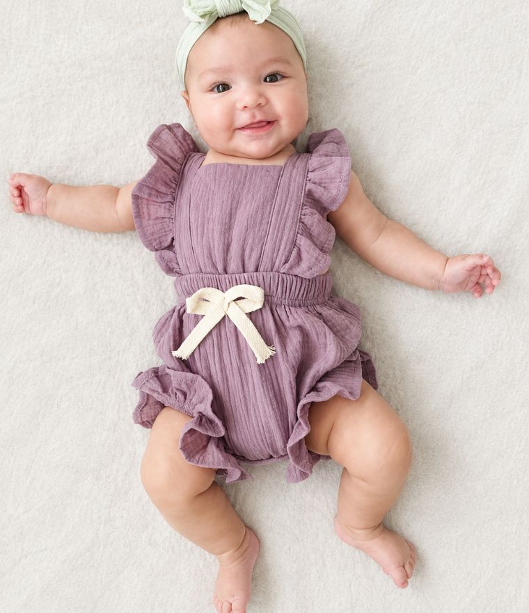 Baby girl wearing purple ruffle romper laying on bed