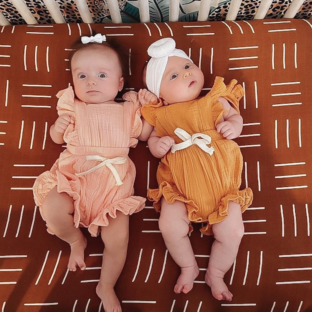 Two babies in cot wearing ruffle rompers in pink and mustard