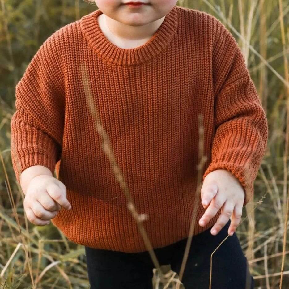 Toddler wearing a cosy, oversized chunky knit jumper in rust outdoors