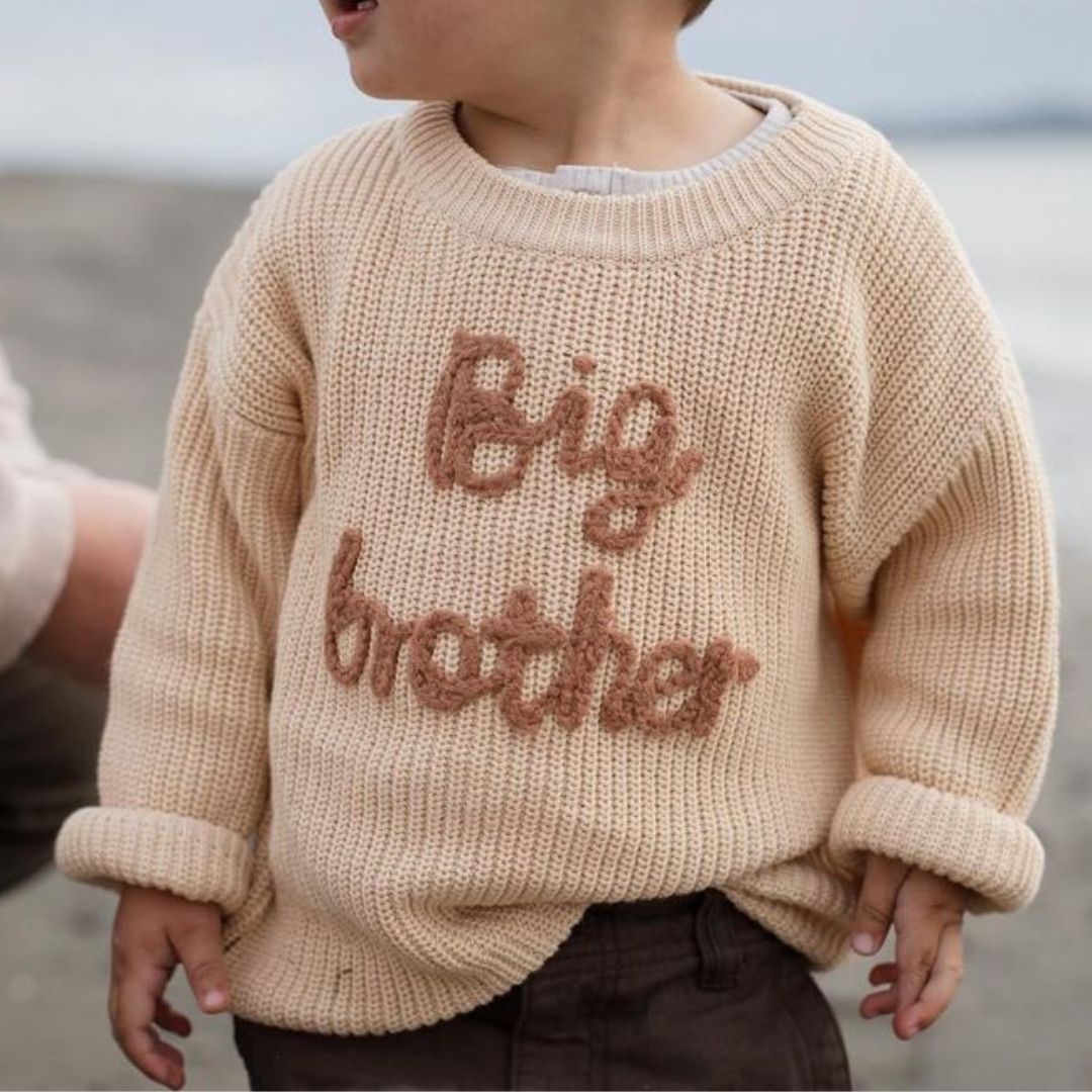 Toddler boy modelling a Big Brother knit jumper in beige.