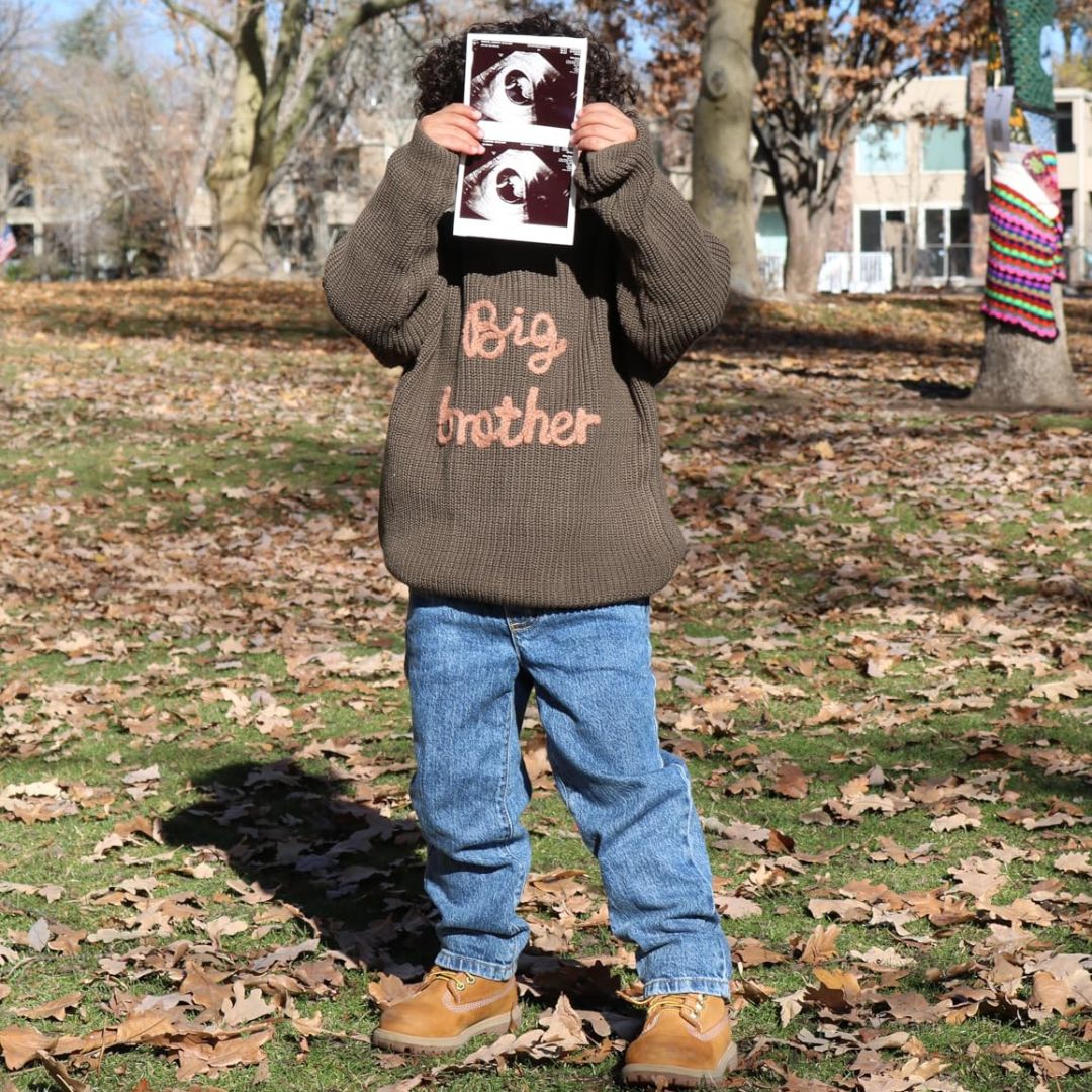 Boy wearing big brother jumper, holding up ultrasound photos to announce a pregnancy