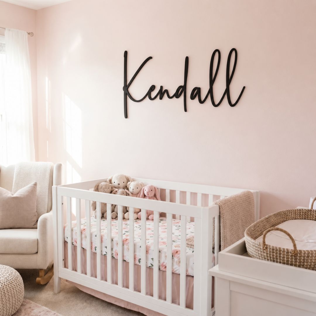 Personalised black acrylic name sign with the name "Kendall" in cursive font, hanging above a baby cot