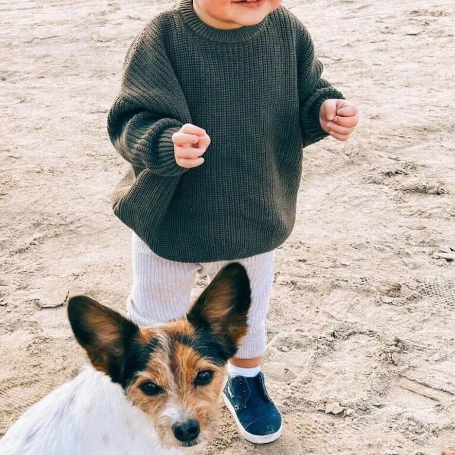 Toddler wearing chunky knit olive jumper with relaxed fit, walking along beach