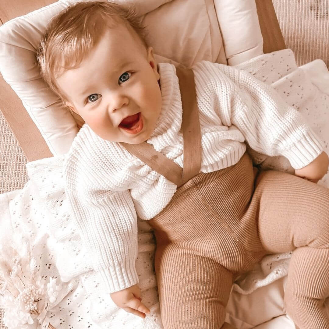Cute baby boy wearing a white knitted jumper and suspender tights in latte - an adorable winter outfit