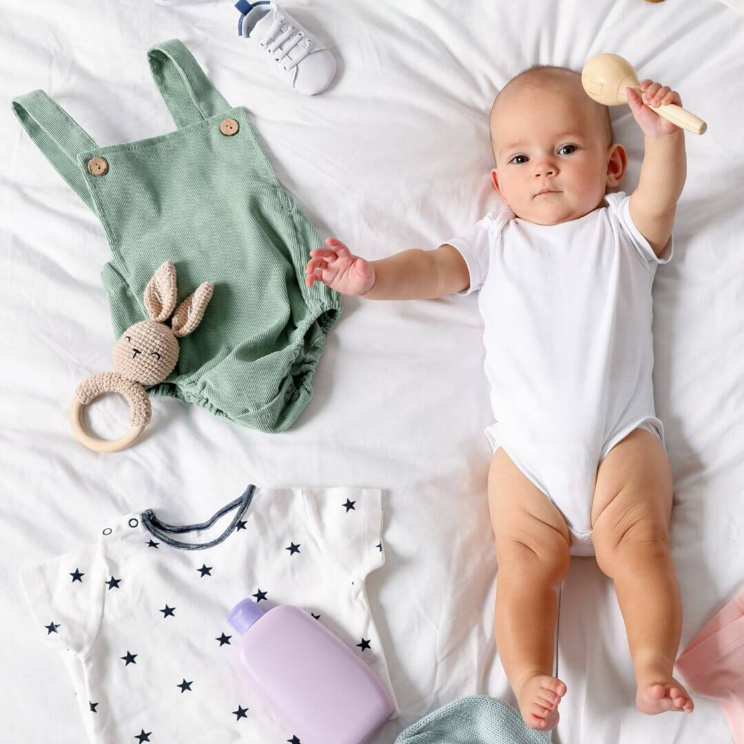 Baby lying on bed with baby clothes
