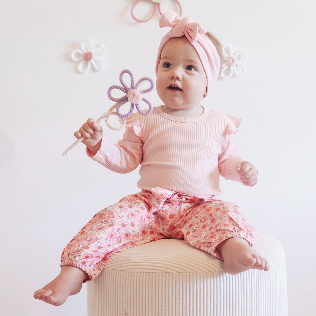 Baby girl modelling pink floral baby girl outfit - ribbed flutter romper, floral pants & matching headband