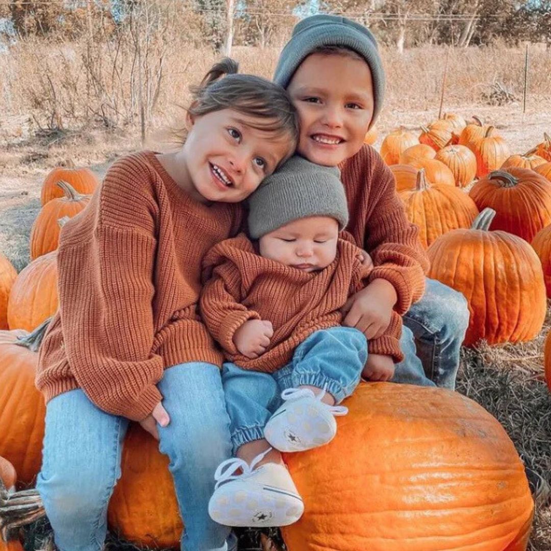 Siblings wearing matching knitted baby jumpers in rust