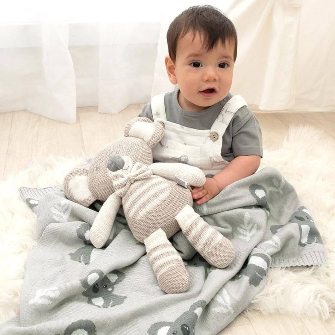 Adorable baby sitting on a grey koala baby blanket, showcasing the cozy 100% cotton knit design.