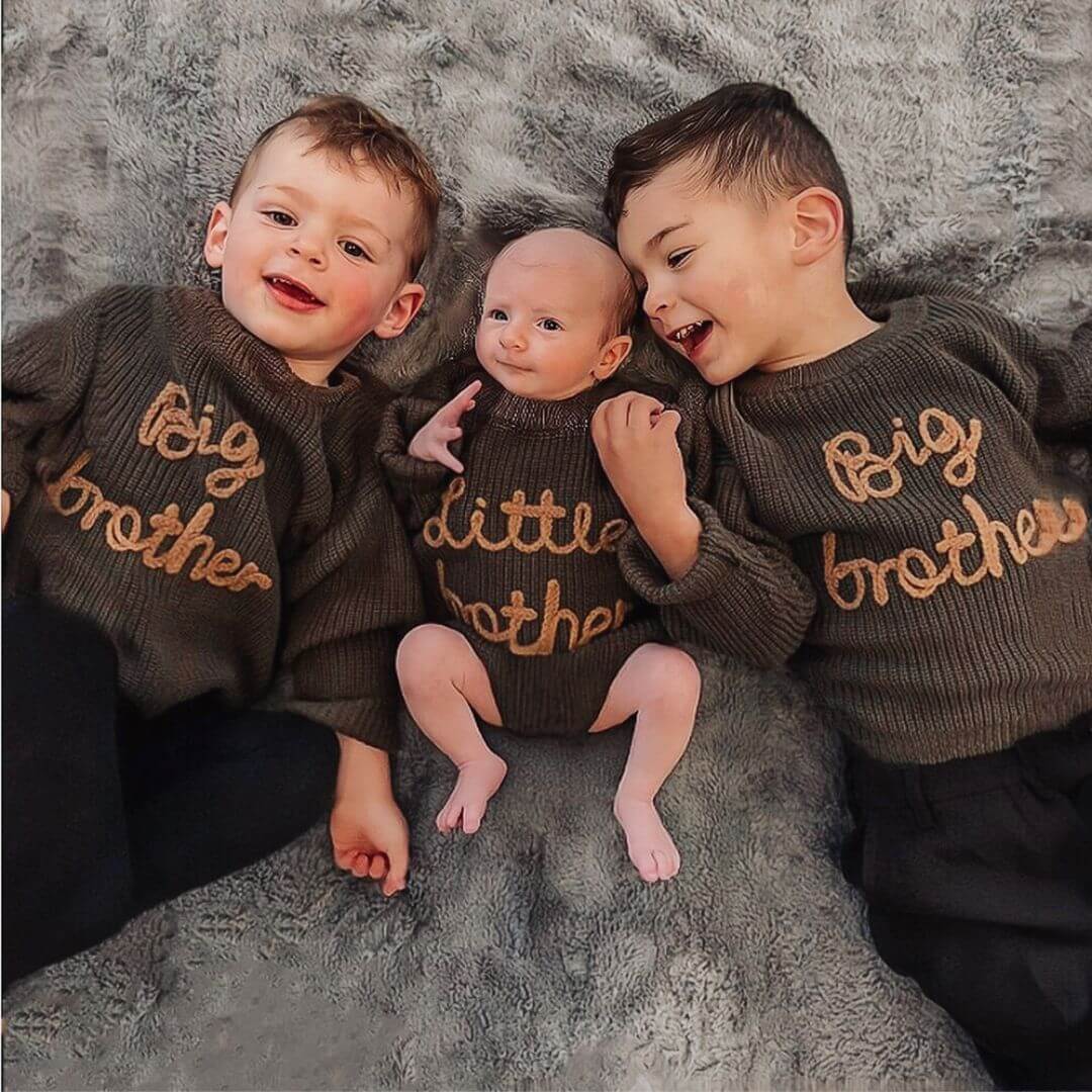 Three brothers lying on a bed wearing matching Big Brother Little Brother jumpers