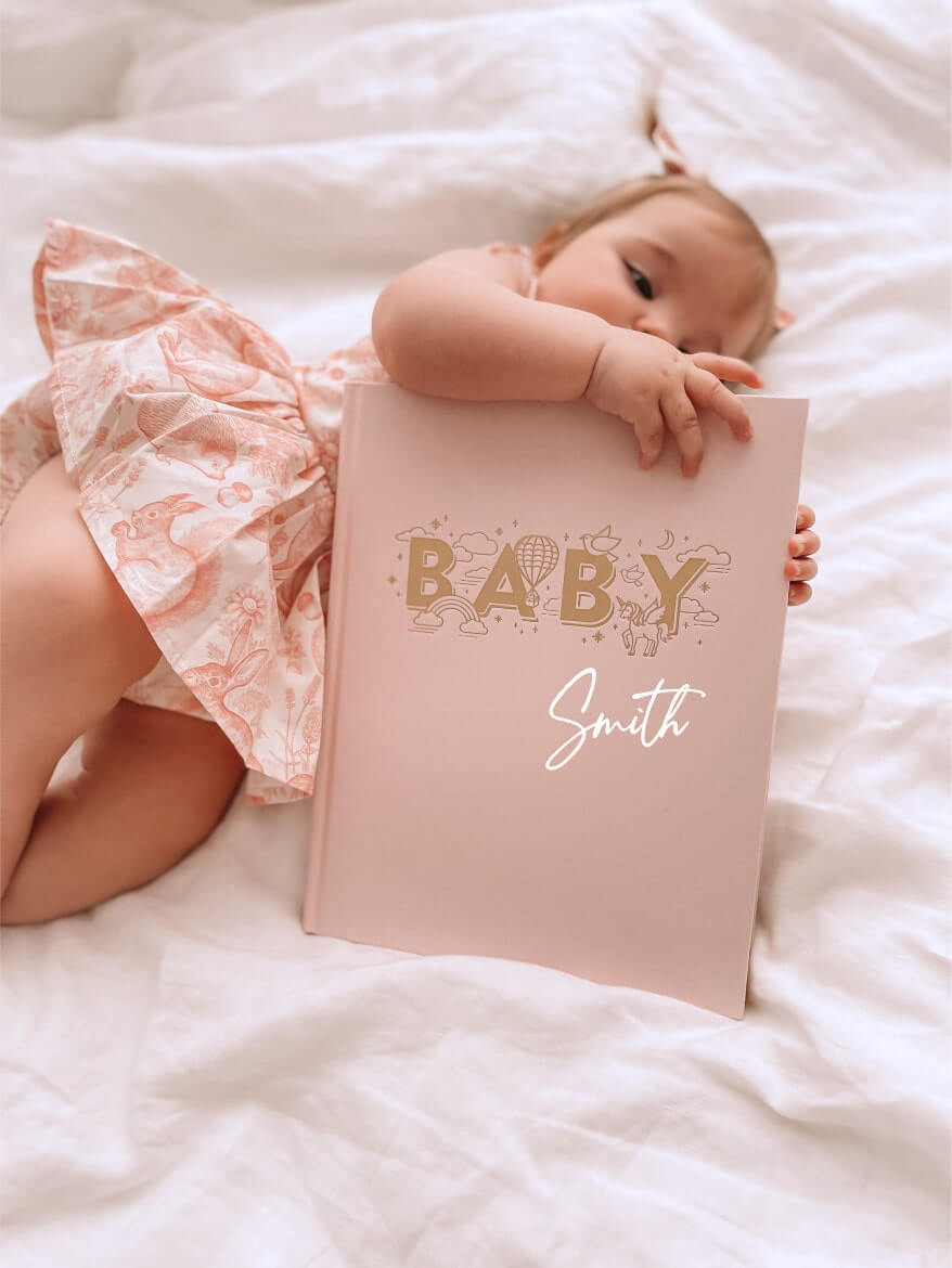 Baby girl holding personalised keepsake journal in rose, for recording milestones and memories