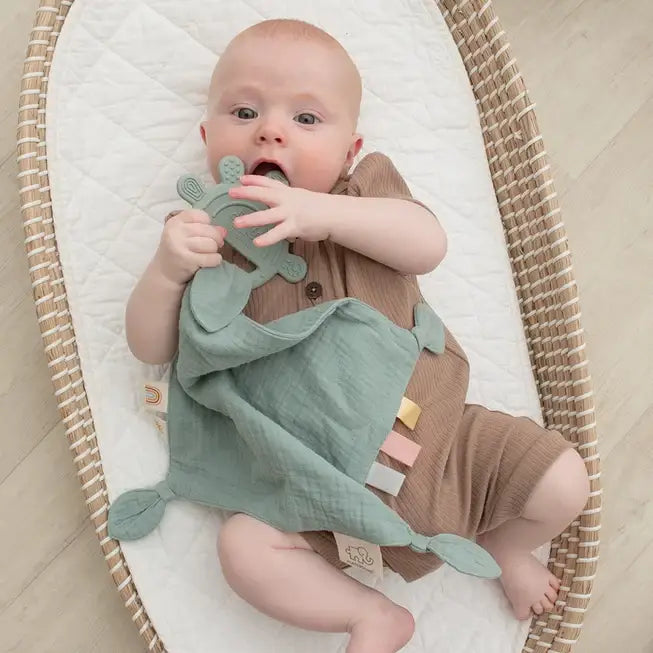 Baby playing with a personalised silicone teether and soft muslin comforter, perfect for teething relief. Baby gift idea.
