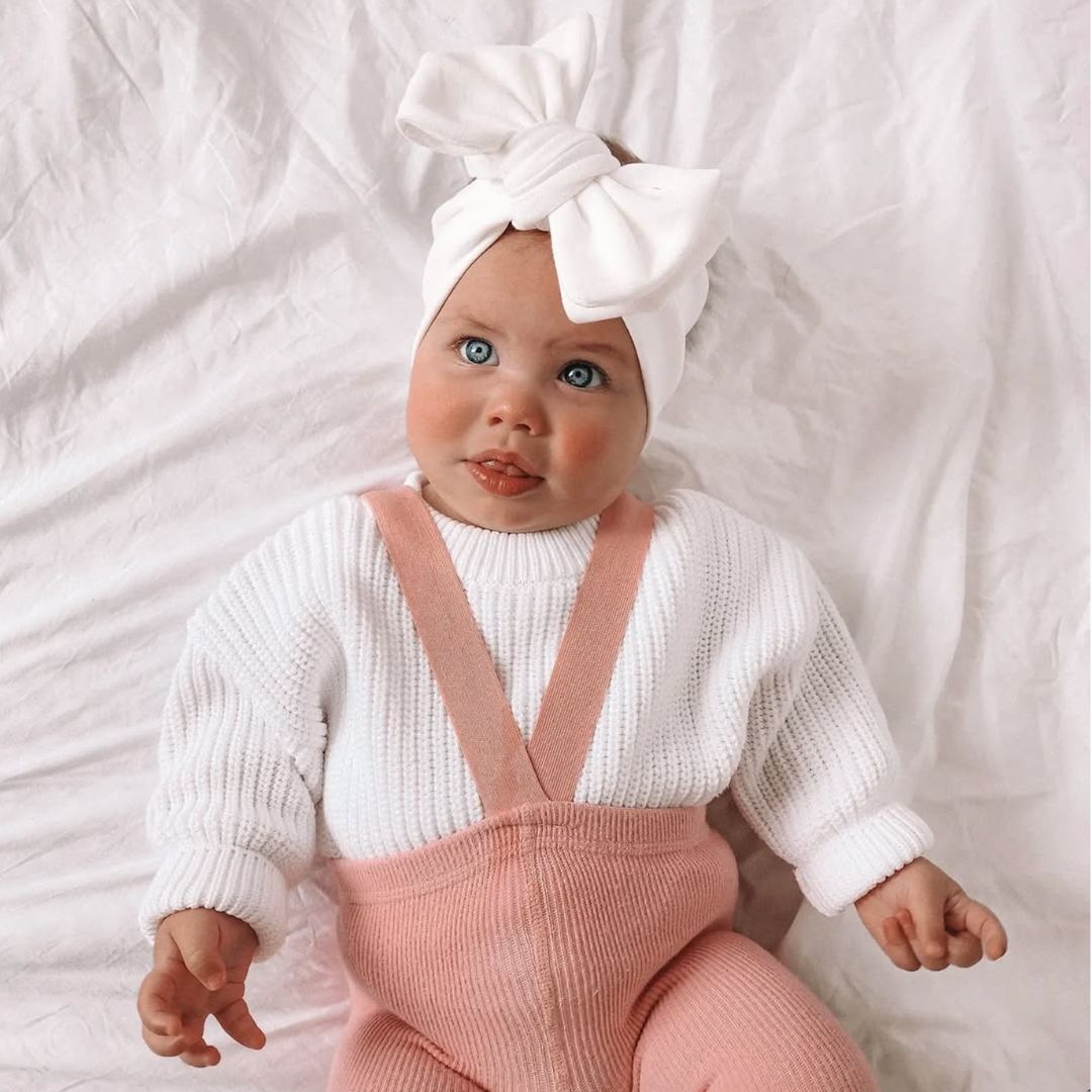 Baby girl wearing white knit oversized baby jumper and pink suspender tights