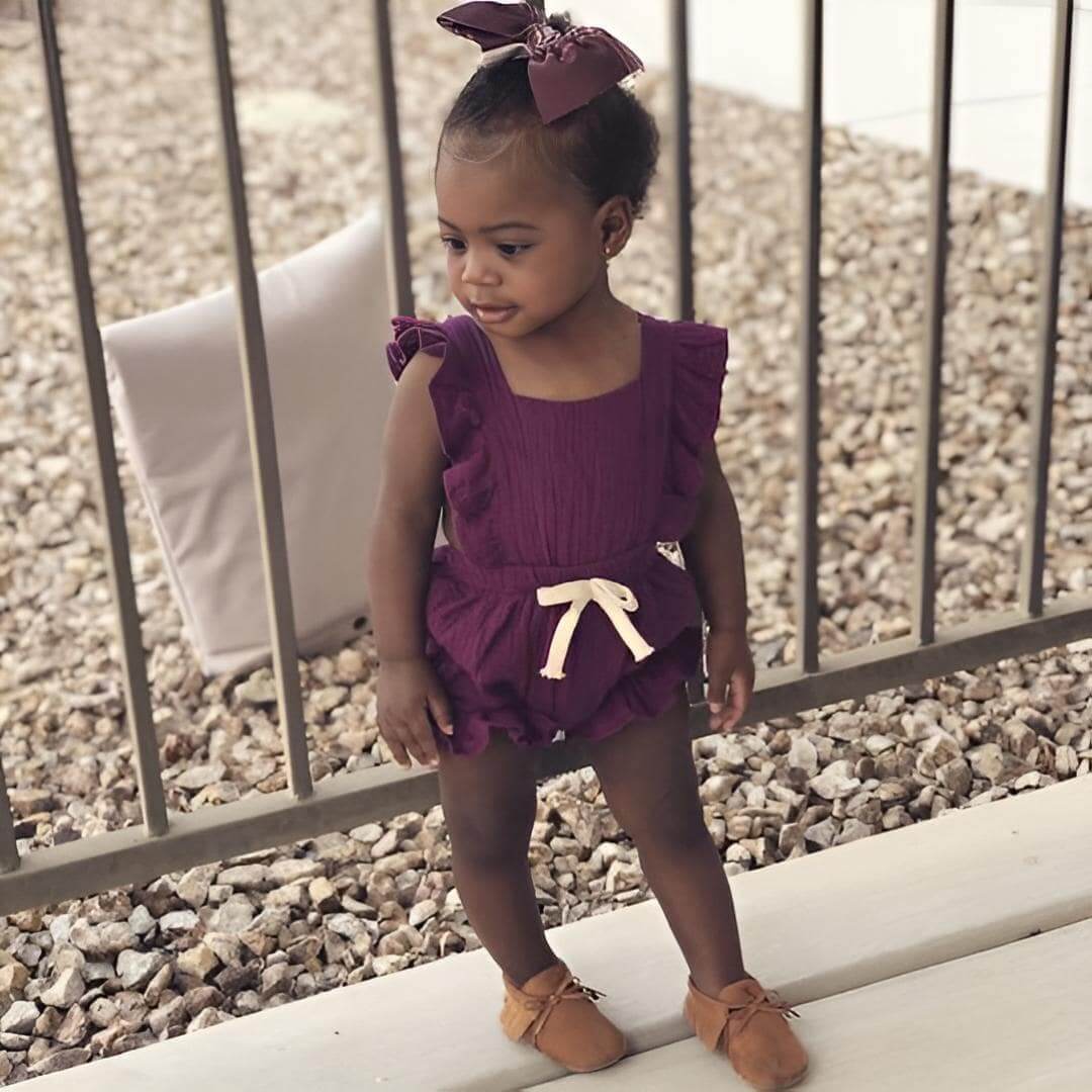 Toddler girl wearing burgundy Willow ruffle romper outdoors
