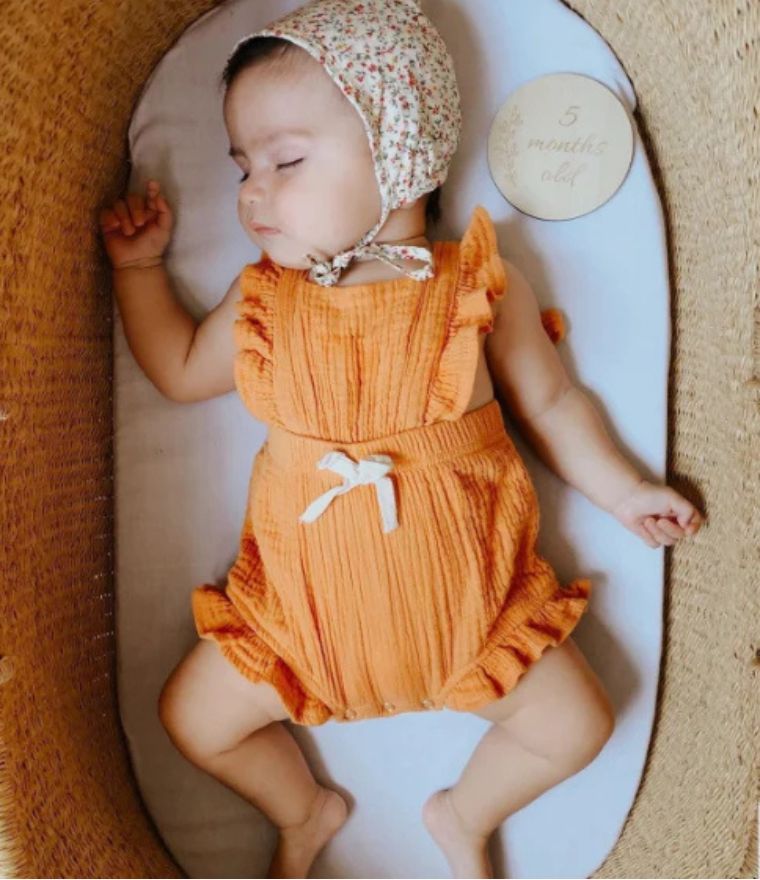 Sleeping baby girl wearing ruffle baby romper in mustard