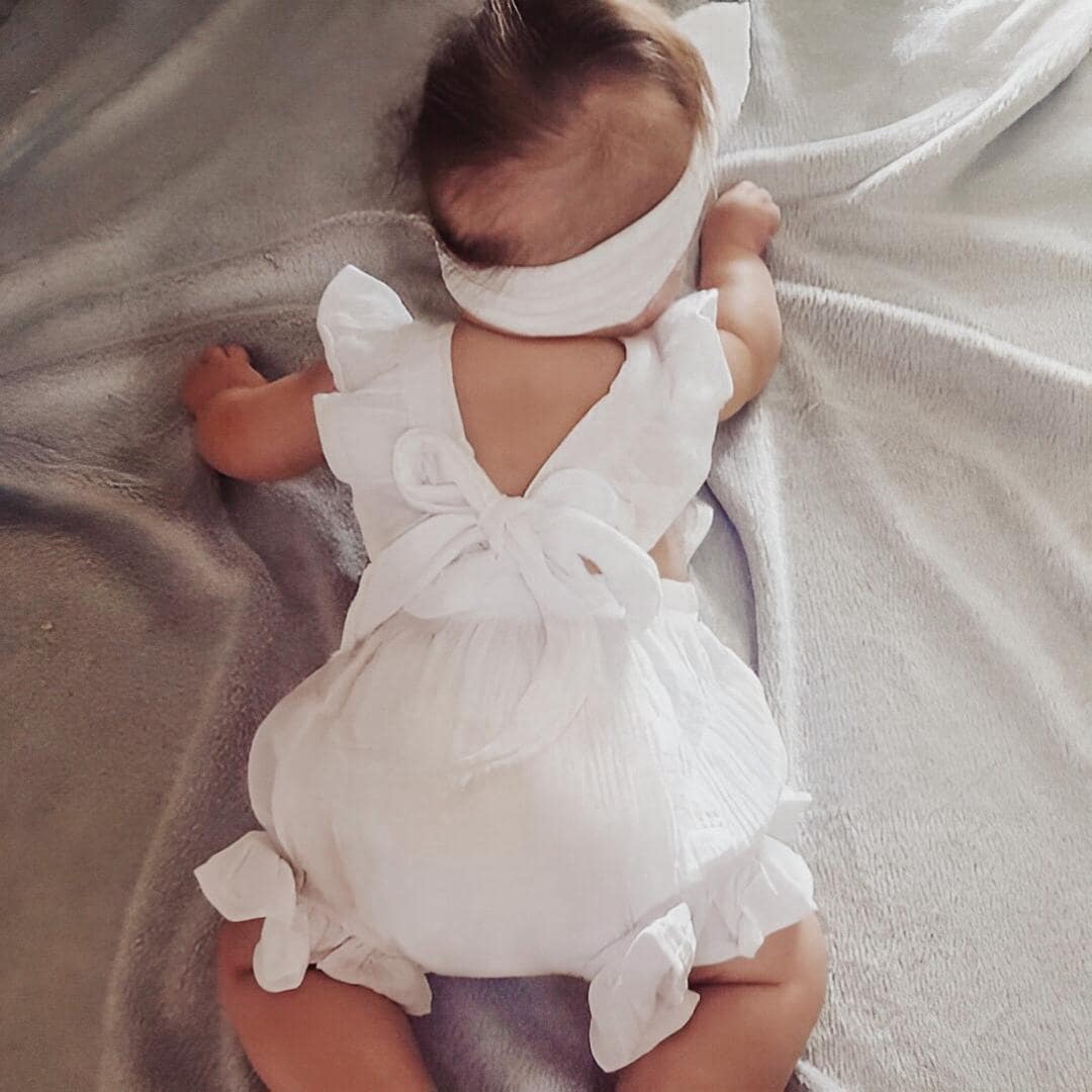Baby wearing white Willow Ruffle Onesie - crawling on bed
