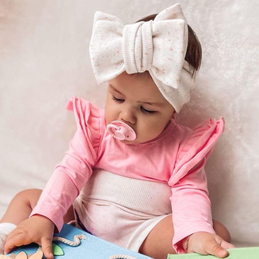 Baby girl wearing pink long sleeve flutter bodysuit, sitting and reading