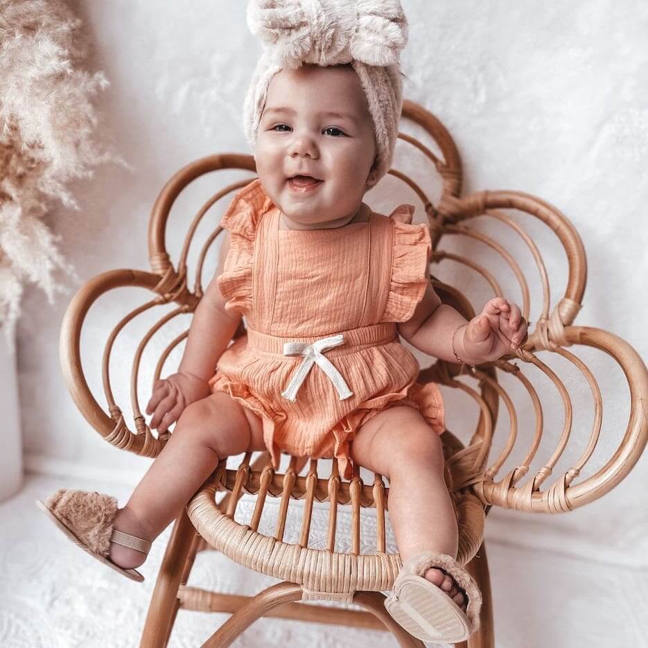 Smiling baby girl wearing our pink Willow Ruffle Baby Romper with our fluffy baby slides in brown