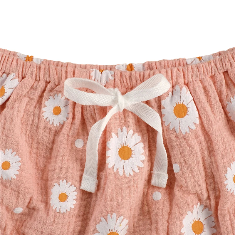 Close-up of the soft pink fabric featuring cheerful daisy print and tie detail, part of the Daisy Ruffle Peplum Set.