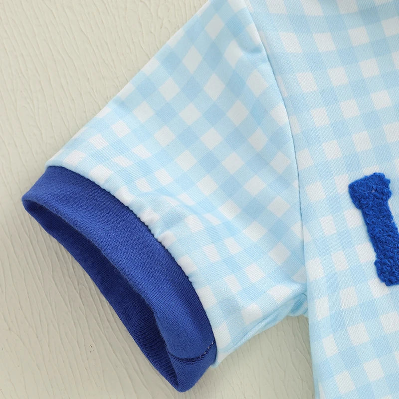 Close-up of blue gingham romper sleeve with dark blue trim and embroidered detail for boys' clothing.