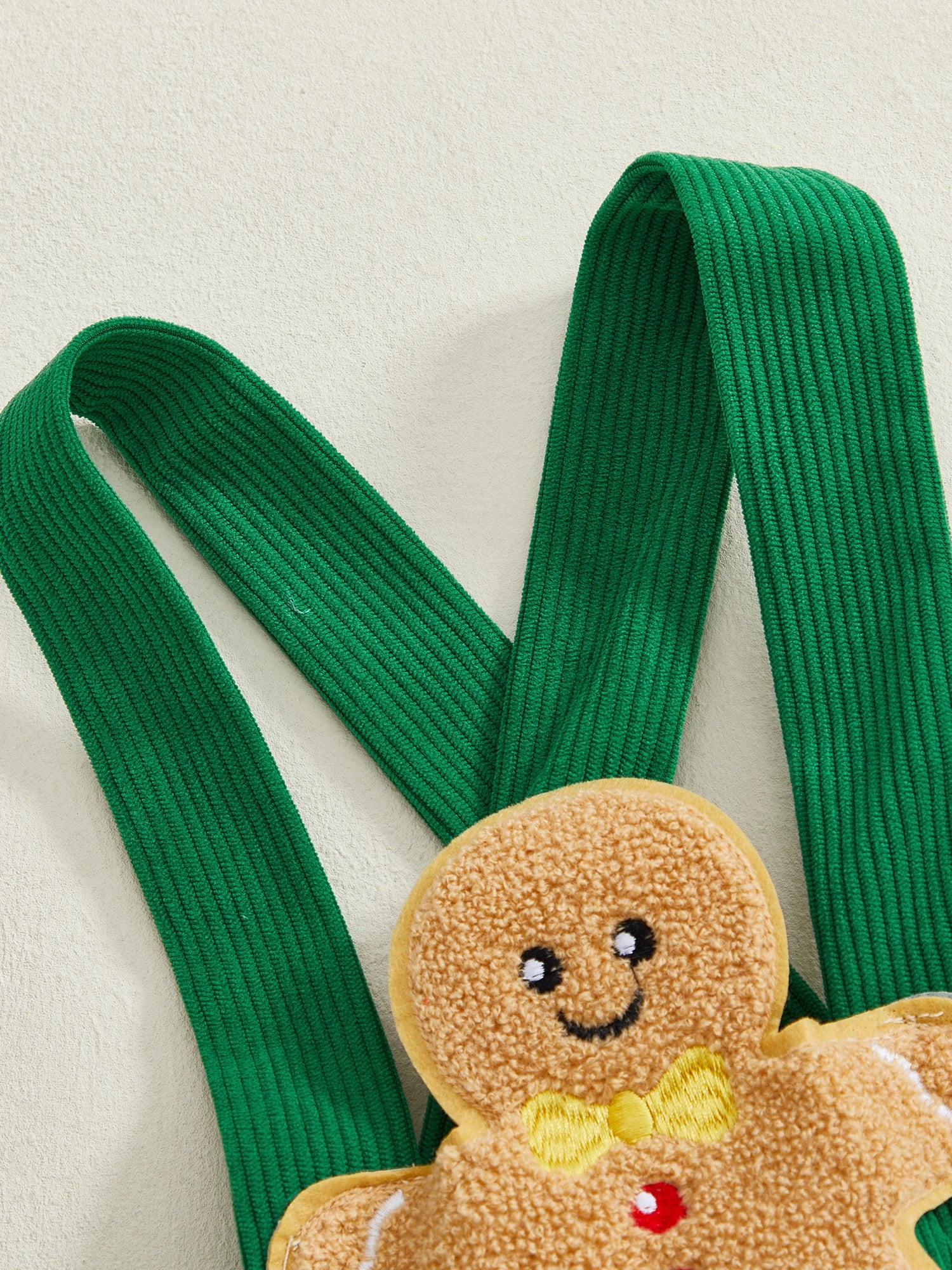 Green corduroy straps of a gingerbread man romper with a sweet gingerbread man appliqué for Christmas celebrations.