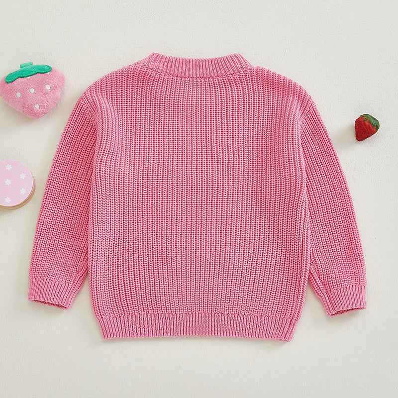 Pink chunky knit Big Sis jumper with embroidery script and strawberry appliqués, flat lay on cream background