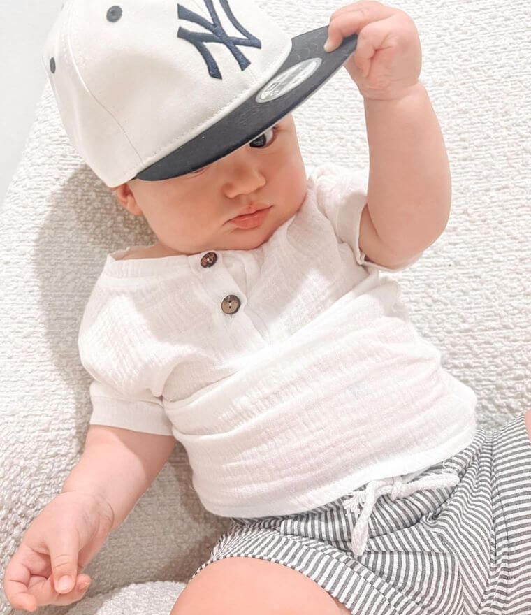 Baby boy in Arlo baby outfit with cap: white muslin top and pinstripe shorts