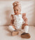Adorable baby girl wearing a stylish Lulu Babe outfit with a pink turban headband, white ruffled top, and brown shoes, showcasing cute children's clothing.