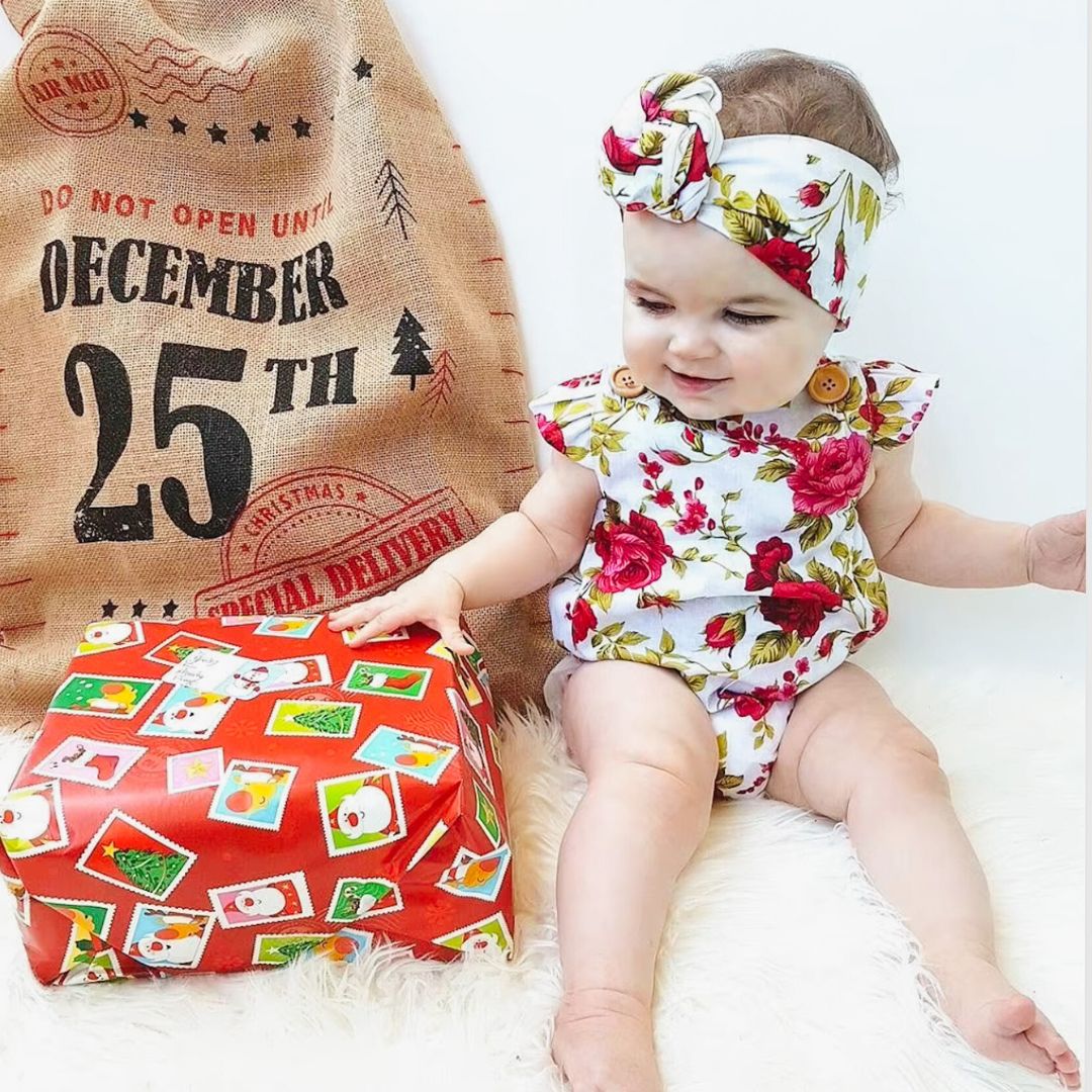 Baby girl wearing Ava floral romper in red and white with Christmas present