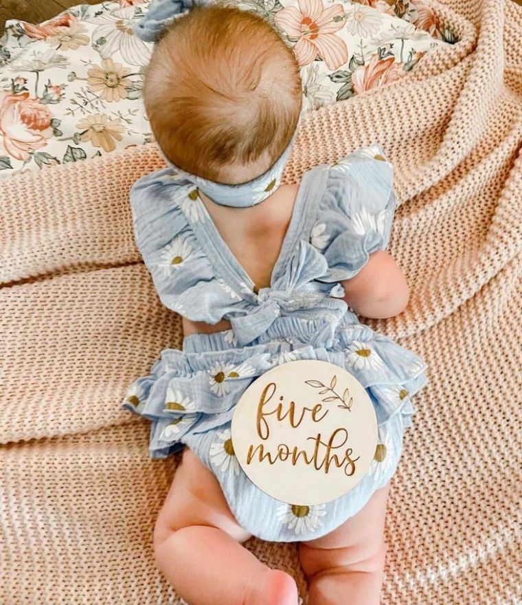 Baby girl wearing our Daisy Ruffle Romper in blue, showing the back