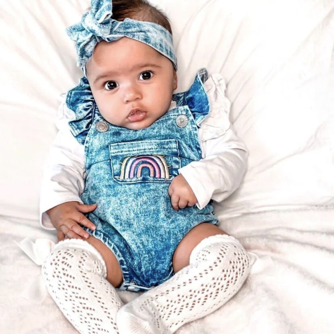 Baby girl wearing Denim Ruffle Rainbow Romper, layered over long sleeve romper