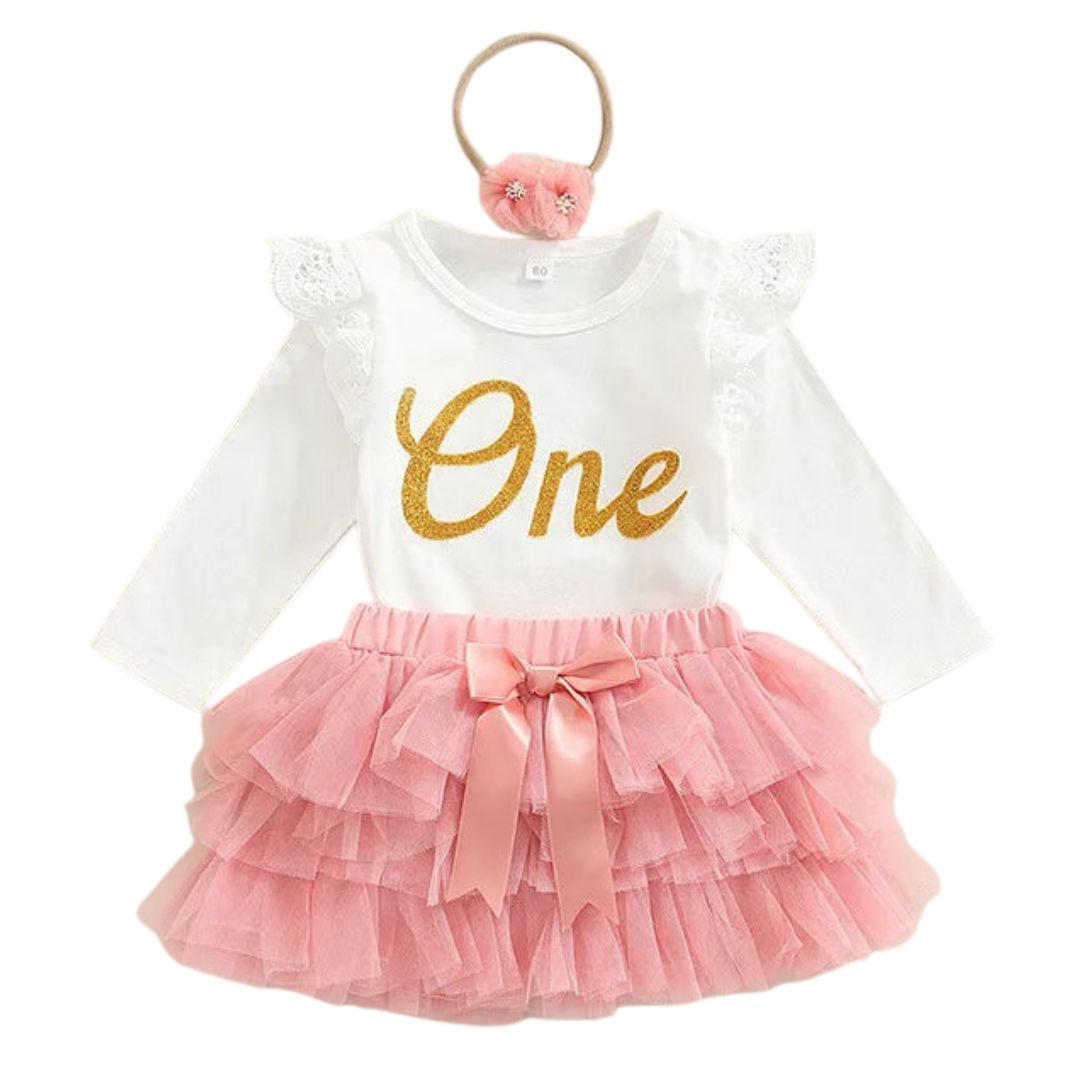 Baby girl first birthday tutu set – white long-sleeve "One" bodysuit with gold glitter print, pink layered tulle skirt with satin bow, and floral headband