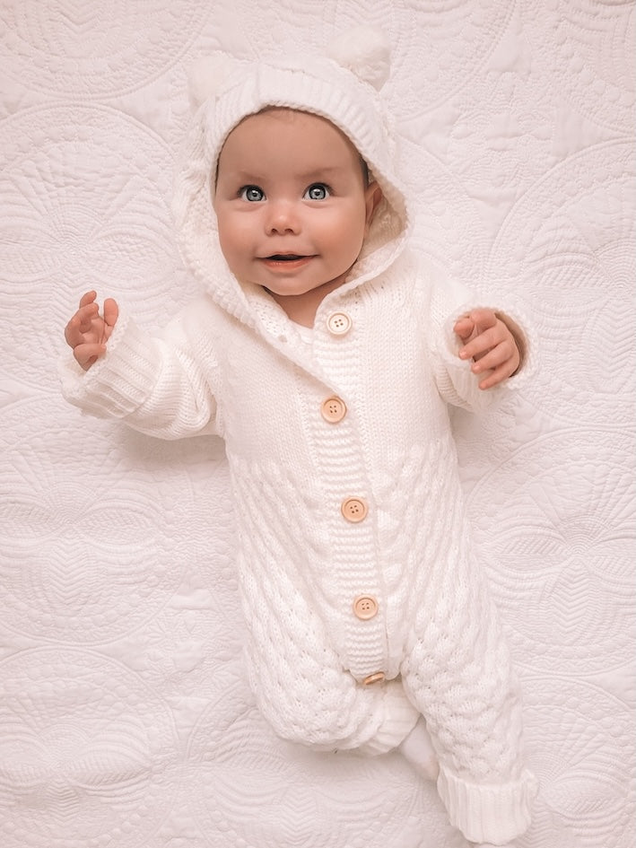 Baby wearing our white knitted teddy bear onesie with pom-pom ears. Adorable and cozy baby outfit.