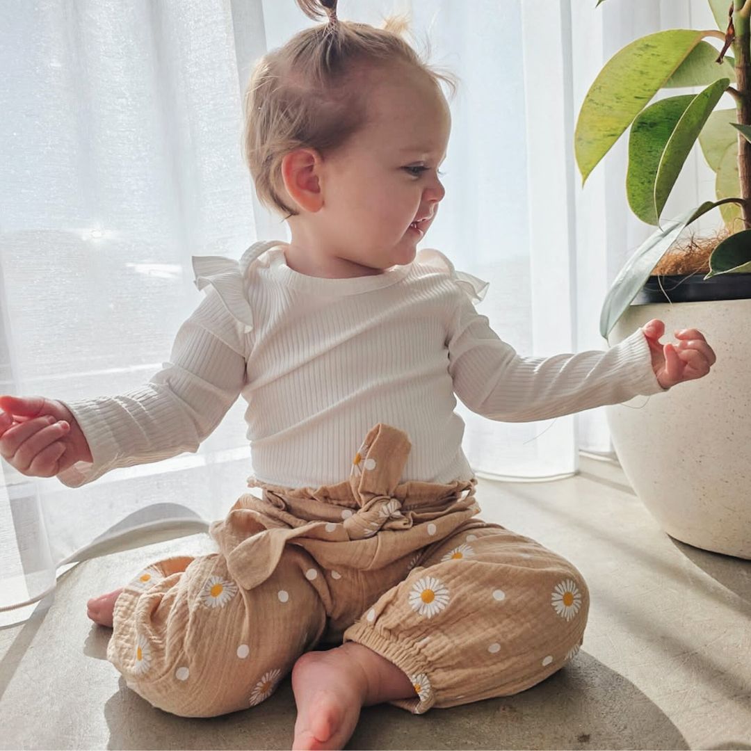 Baby girl wearing daisy muslin pants set in beige - indoors