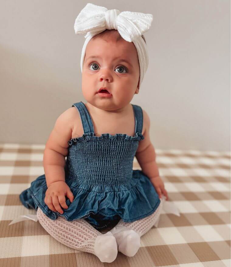 Sitting baby girl wearing Denim Peplum Romper and knee high socks
