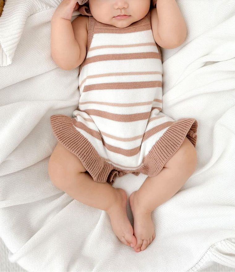 Baby girl wearing sleeveless knit romper in beige and white stripes with ruffle detail.