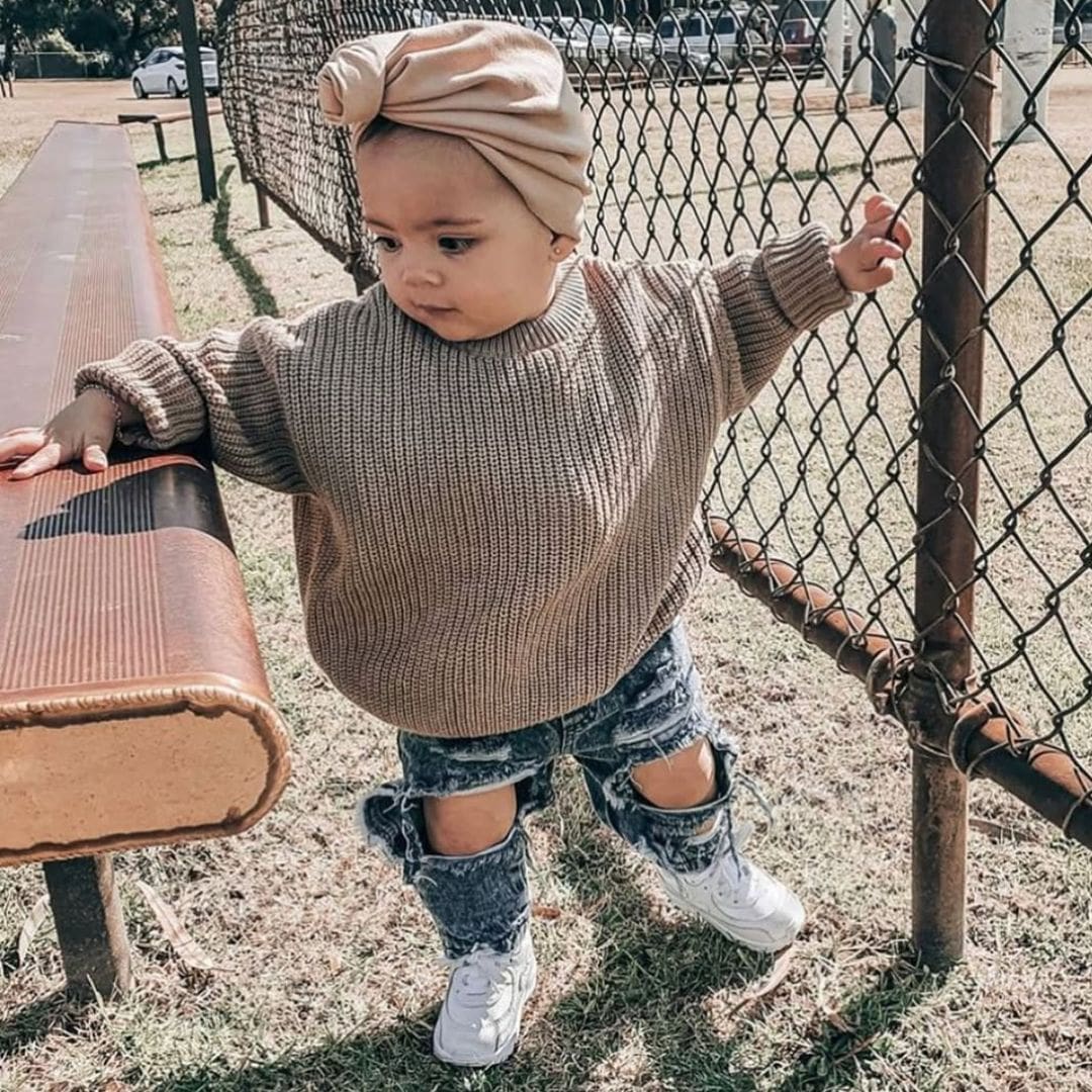Baby girl wearing our chunky knit jumper in taupe & distressed denim jeans