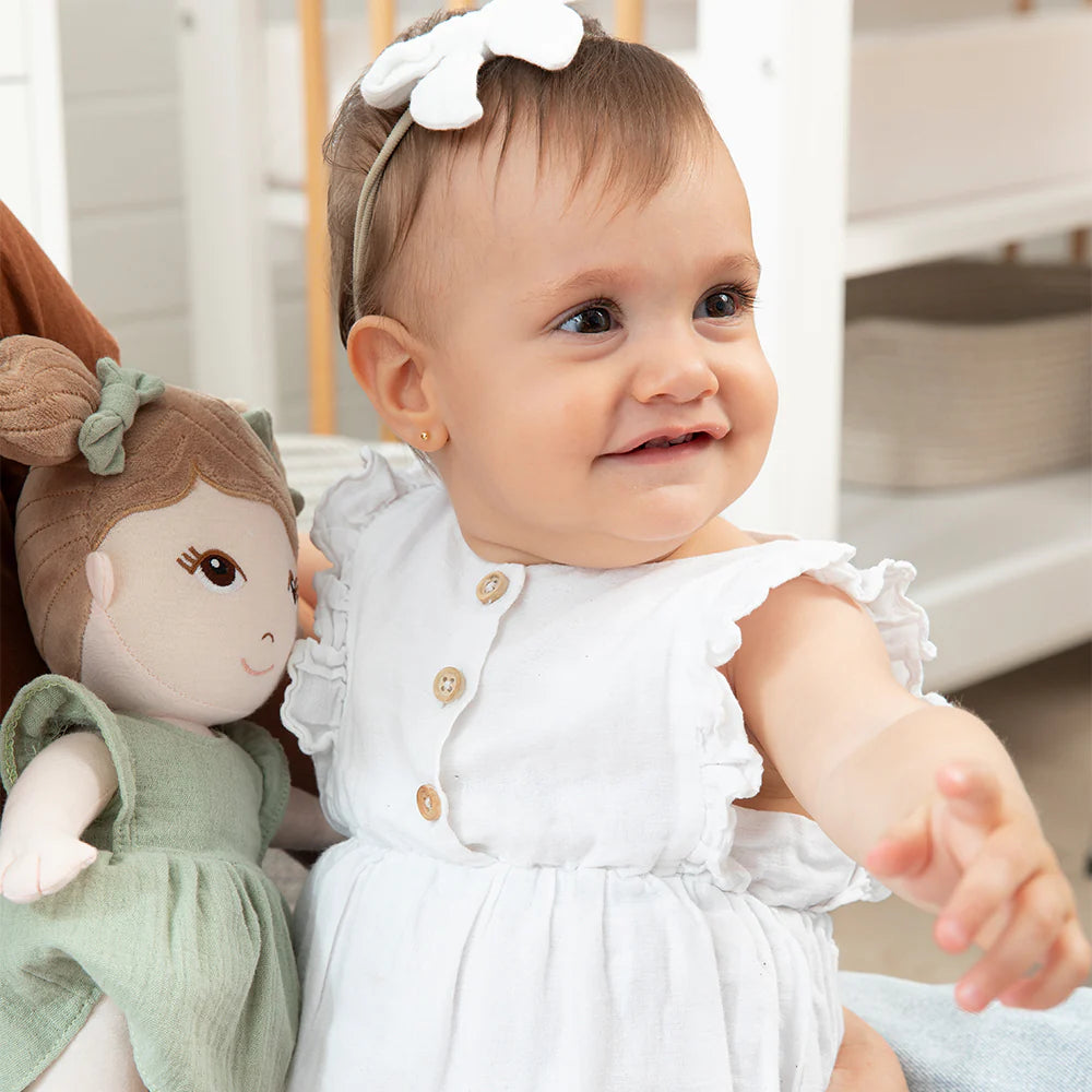 Baby doll cuddled by a happy baby in a white dress