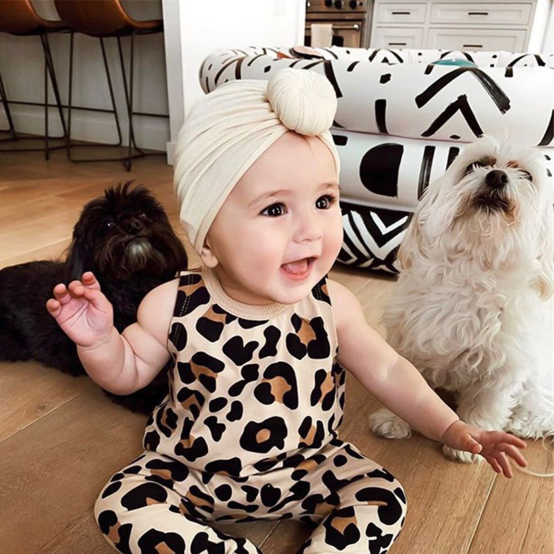 Smiling baby girl wearing an Olivia top knot turban in beige.