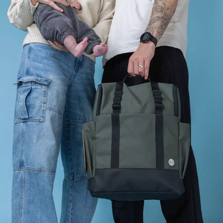 Parents holding baby with Babymel Finn nappy backpack in olive.