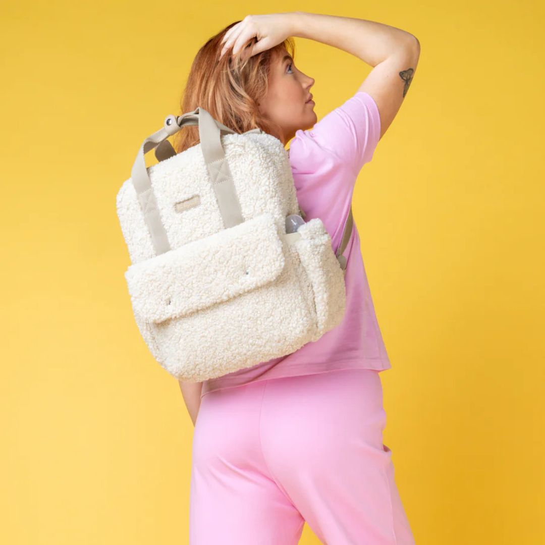 Mum wearing Babymel Teddy Cream Nappy Backpack against a bright yellow background.
